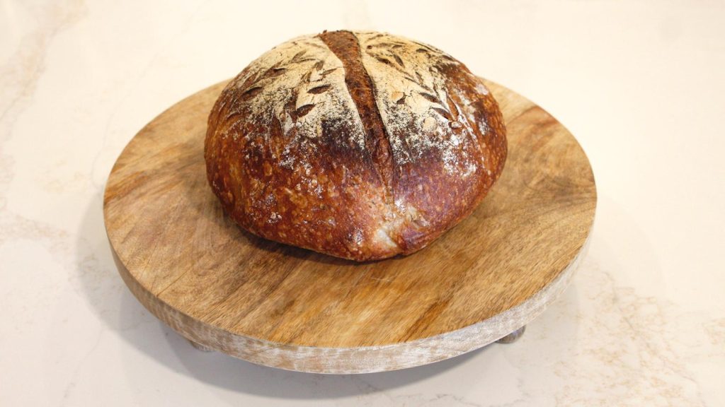 Whole sourdough loaf with wheat scoring on a round wooden board